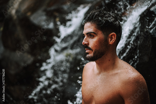 hombre bajo una cascada en plena naturaleza disfrutando de una ruta en su viaje de vacaciones