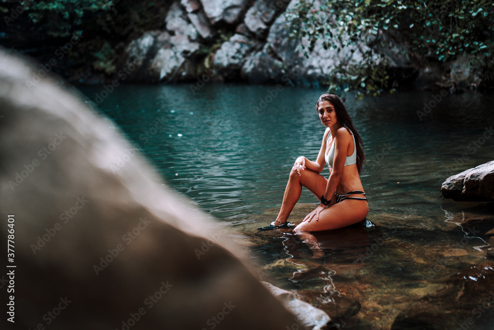 Chica atractiva morena sobre roca en lago