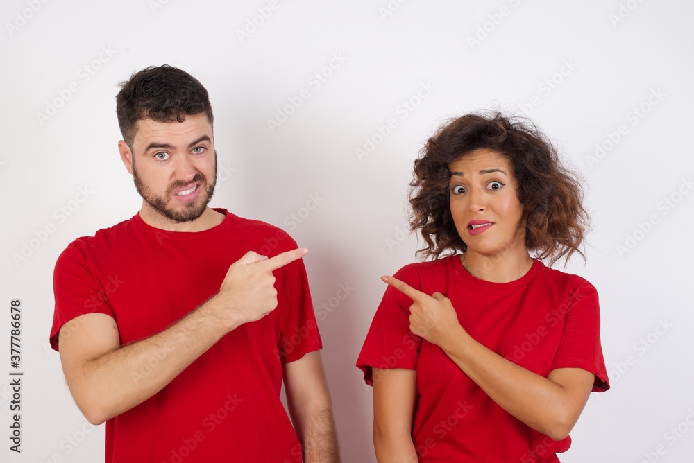 Young beautiful couple wearing red t-shirt on white background Pointing aside worried and nervous with forefinger, concern and surprise concept. Young beautiful couple wearing red t-shirt on white background Pointing aside worried and nervous with forefinger, concern and surprise concept.