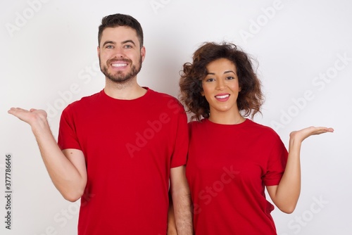 Cheerful cheery optimistic Young beautiful couple wearing red t-shirt on white backgroundholding two palms copy space photo