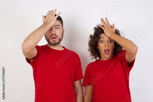 Konstfotografi Young beautiful couple wearing red t-shirt on white background surprised with hand on head for mistake, remember error