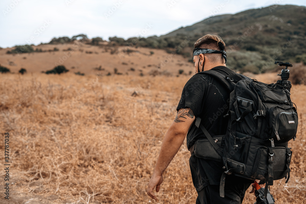 Joven explorador fotografo camina por medio de un valle seco en la naturaleza con su equipo fotografico Joven explorador fotografo camina por medio de un valle seco en la naturaleza con su equipo fotografico