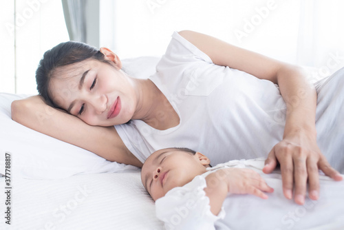 Loving mom carying of her newborn baby at home. Bright portrait of happy mum holding sleeping infant child on hands. Mother hugging her little. Mother and her baby son  sleeping on a big bed.
