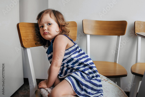 child girl sitting on a chair and looking sadly at the camera. photo