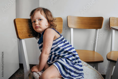 Photos child girl sitting on a chair and looking sadly at the camera.
