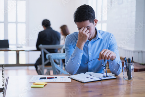 Billede på lærred Young asian businessman feeling stressed and massaging his nose and keeping eyes closed