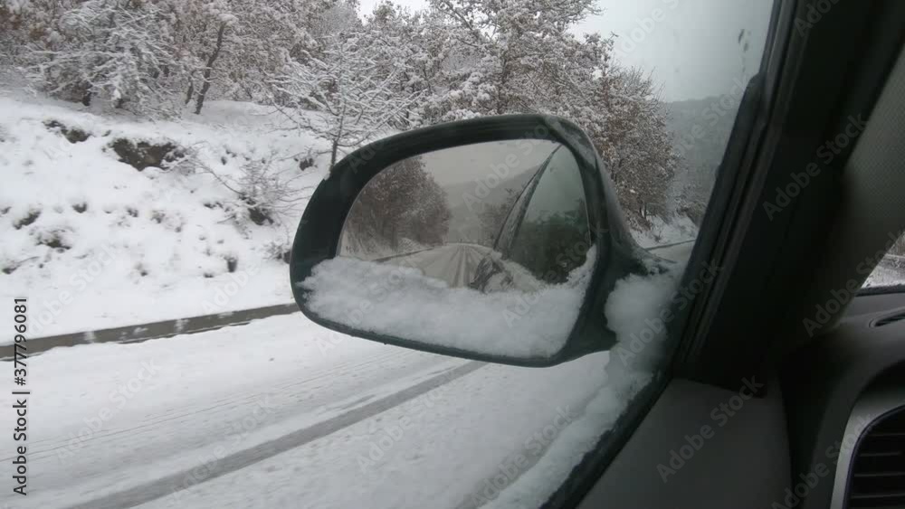Car driving on snow-covered snowy mountain road in winter snow. Driver`s point of view viewpoint looking through side mirror Car driving on snow-covered snowy mountain road in winter snow. Driver`s point of view viewpoint looking through side mirror