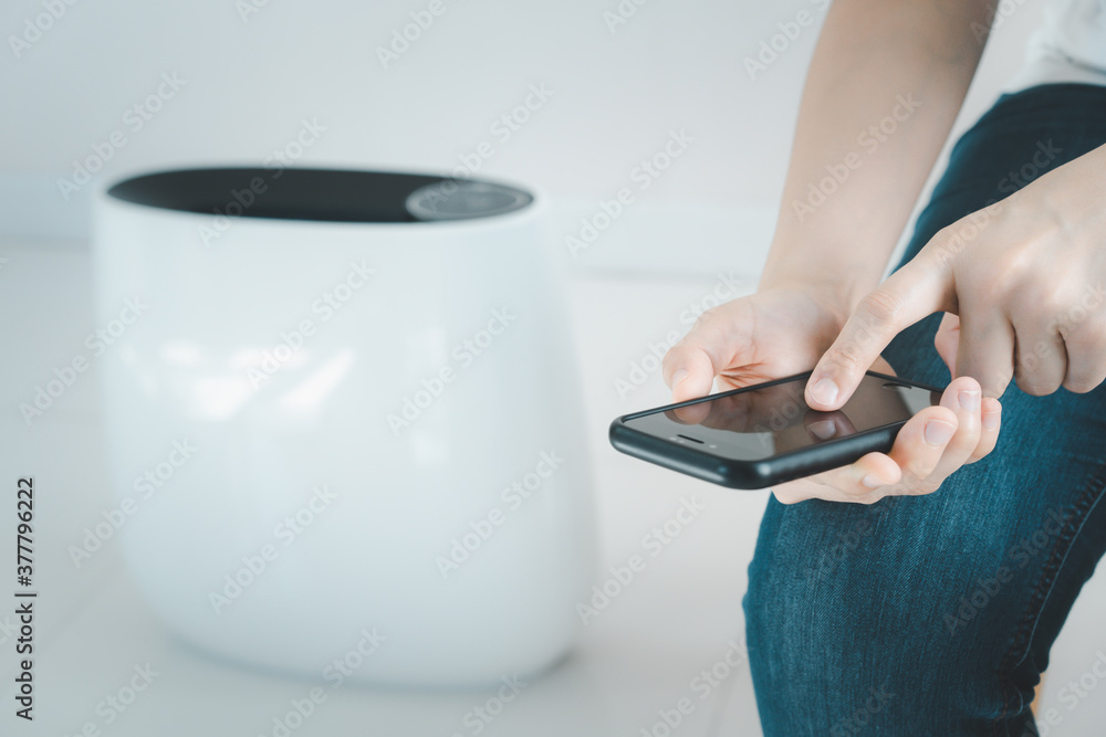 Fototapeta premium Woman control a modern air purifier through the application on a smartphone, a smartphone screen isolated in white color. Modern and smart home connectivity technology concept.