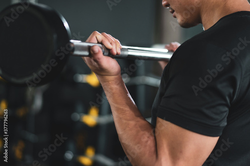 Powerful sportive man lifting up a heavy barbell in a gym, body building exercise. 
