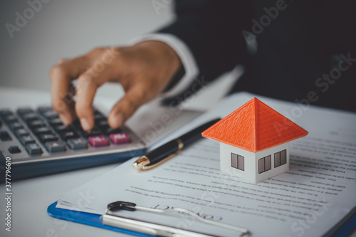  Businesswoman calculating budget before signing real estate project contract with house model at the table in the office, Bank calculates the home loan rate.