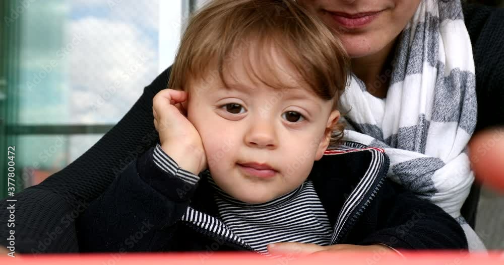 Close-up baby toddler face watching cellphone screen on mother lap. Infant communicating with family member over video Close-up baby toddler face watching cellphone screen on mother lap. Infant communicating with family member over video