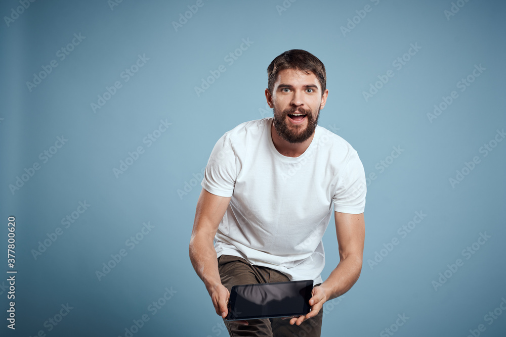 Energetic man with a touch tablet on a blue background in a white t-shirt cropped view Energetic man with a touch tablet on a blue background in a white t-shirt cropped view