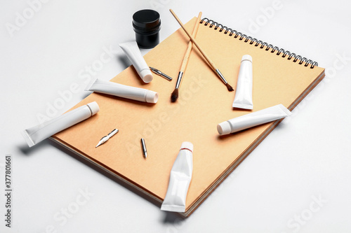 Notebook with paints and brushes on white background