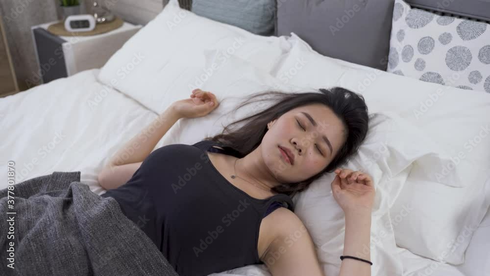 portrait of asian lady nearly waking up in the morning before the alarm going off. chinse woman in black tank top moving about in bed while sleeping portrait of asian lady nearly waking up in the morning before the alarm going off. chinse woman in black tank top moving about in bed while sleeping
