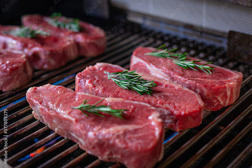 Many Fresh New York Strip Cut Beef - Barbeque Meat on a Grill, decorated with Rosemary