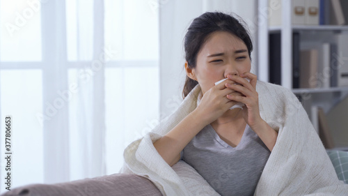 portrait asian female with covid-19 covering mouth with tissue while coughing and rubbing temples to relieve severe headache.