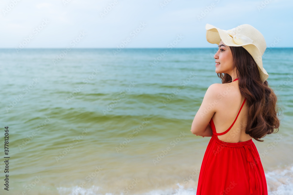 happy woman in red dress standing with arms crossed on sea beach