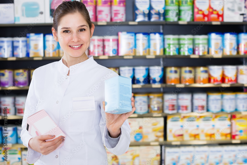 Portrait of young female specialist who is holding medicines near shelves in pharmacy
