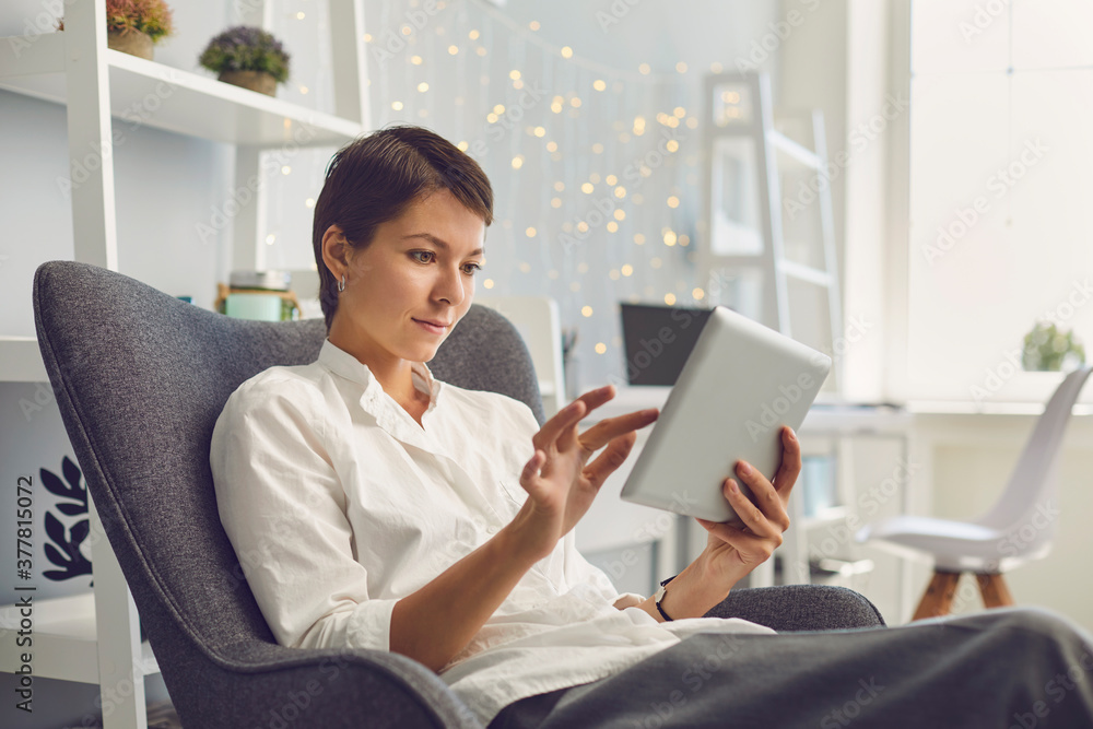 Casual female manager working on tablet sitting in a chair in her office. Casual female manager working on tablet sitting in a chair in her office.