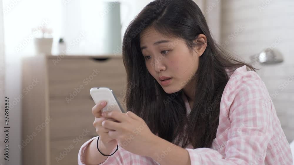 closeup asian lady looking at smartphone screen is sobered up by an astonishing news, and covering her mouth.