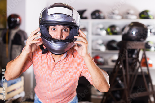 Adult man is trying up new moto helmet for head protection in sport shop