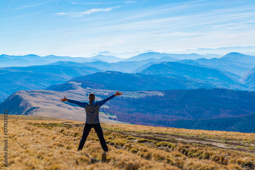 Man with raised arms on the mountain top with a view.