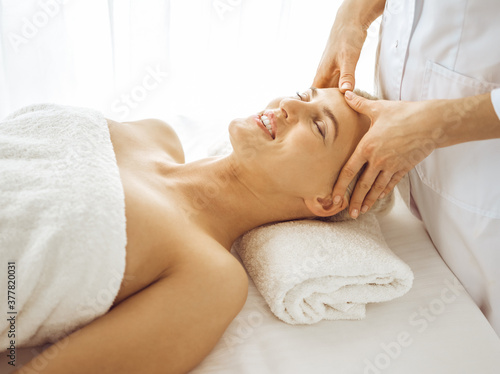 Beautiful blonde woman enjoying facial massage with closed eyes. Relaxing treatment in medicine and spa center concepts