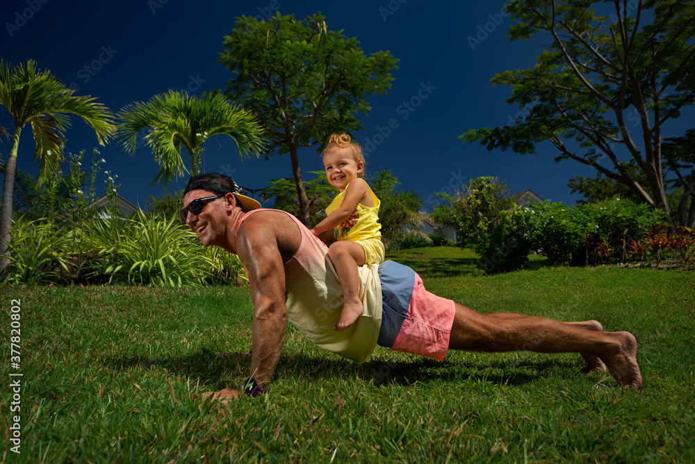 Obraz premium Happy father doing push up exercise with daughter on back in park
