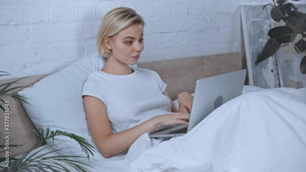 young blonde freelancer typing on laptop in bedroom young blonde freelancer typing on laptop in bedroom