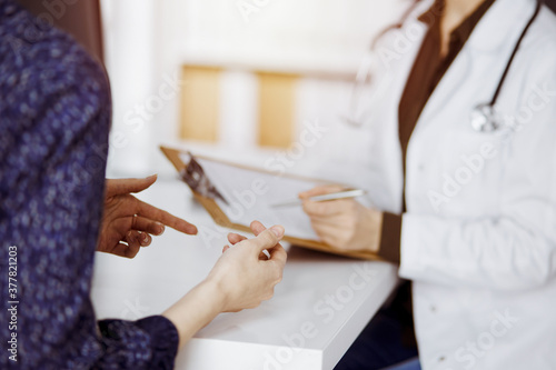 Doctor and patient discussing current health examination while sitting in sunny clinic. Perfect medical service in hospital