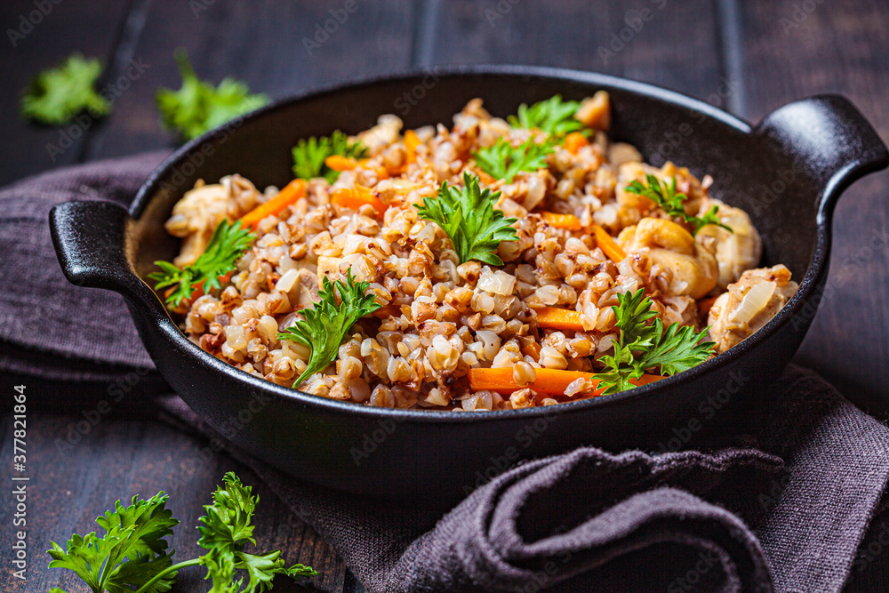 Baked buckwheat with chicken meat and vegetables in black pan, dark background. Traditional Russian cuisine concept.