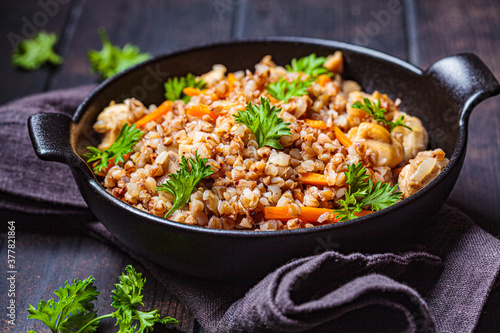 Baked buckwheat with chicken meat and vegetables in black pan, dark background. Traditional Russian cuisine concept.
