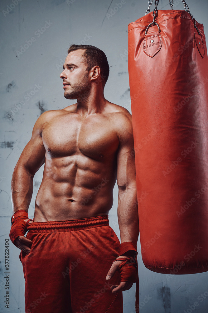 Seductive guy with perfect body and naked torso posing with bandaged hands and punching bag.