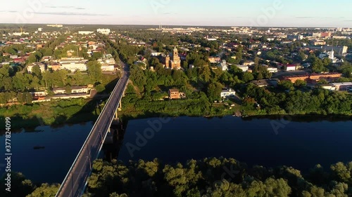 Wallpaper Mural Aerial panorama of the bridge over the river. Dense green trees on the shore. On a hill, there is a church and residential buildings. Cars leave for the road. Evening golden light from the setting sun Torontodigital.ca