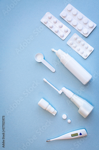 White thermometer, pills, vials with nasal spray and throat spray on blue background