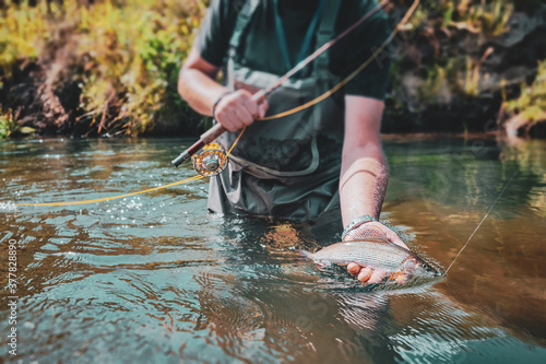 Foto The fisherman holds a grayling in his hand.
