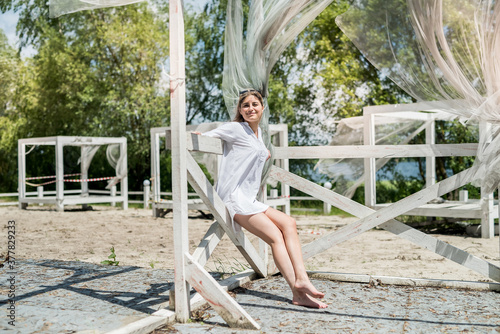 Pretty girl enjoy nature at sunny day in white wooden gazebo near the lake