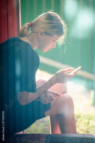 Young girl sitting on the porch of a house in a hot house and looking in the smartphone.