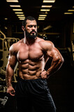 handsome bearded young athlete man with strong muscular physique body in dark sport gym