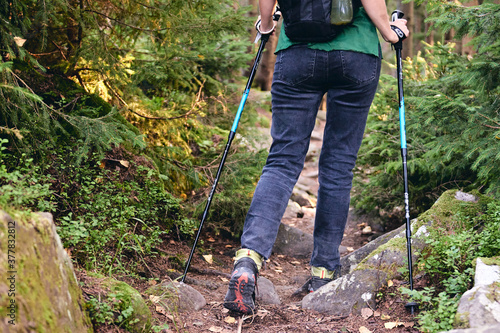 Woman climbs in Hiking boots in outdoor action. Top View of Boot on the trail. Close-up Legs In Jeans And sport trekking shoes on rocky stones of Mountain forest.
