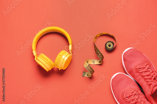 Sportive shoes, measuring tape and headphones on color background