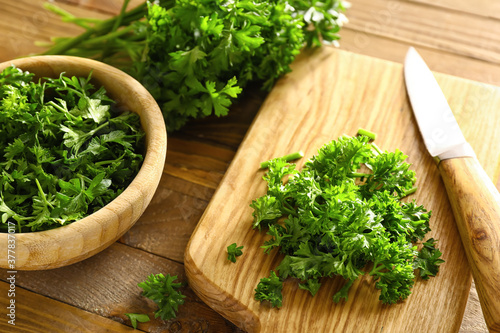 Fresh parsley, bowl, cutting board and knife on wooden background