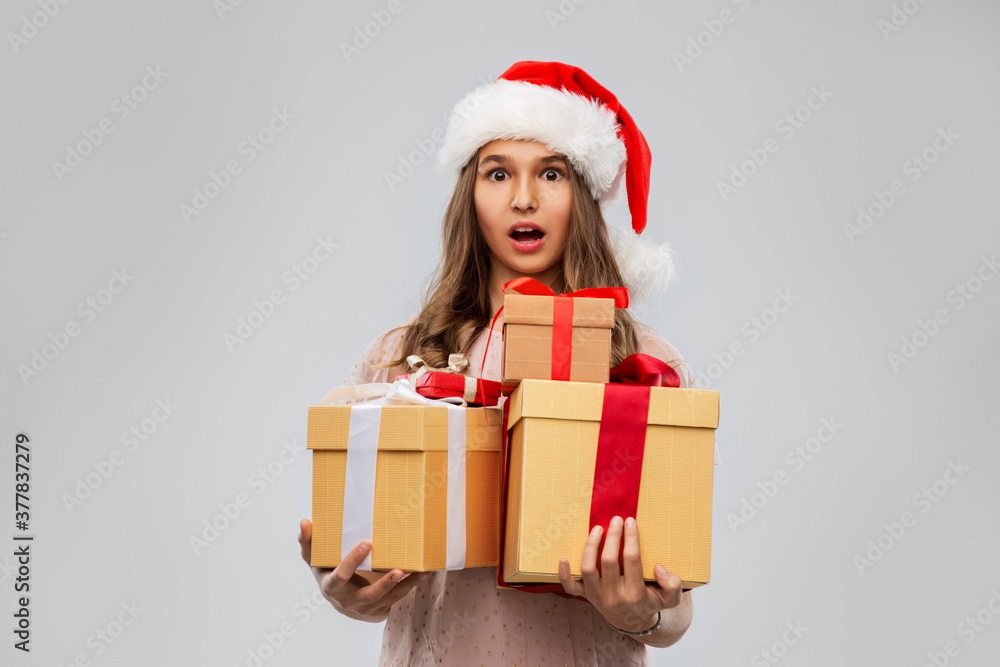 christmas, holidays and people concept - shocked teenage girl in santa helper hat holding gift box over grey background christmas, holidays and people concept - shocked teenage girl in santa helper hat holding gift box over grey background