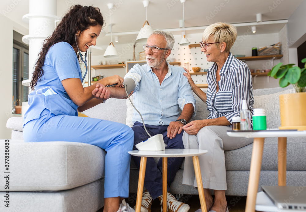 Fototapeta premium Female nurse measures blood pressure to seniors patients while being in a home visit.