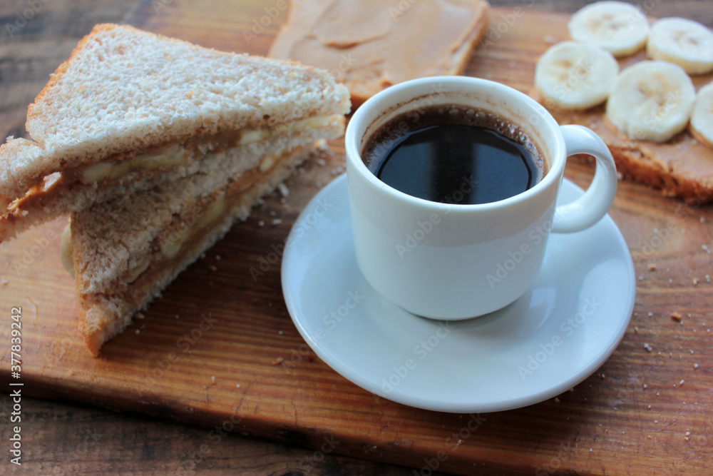 Cup of coffee and peanut butter banana toasts on wooden background. Slices of whole wheat bran bread with peanut paste on a cutting board. Healthy breakfast Cup of coffee and peanut butter banana toasts on wooden background. Slices of whole wheat bran bread with peanut paste on a cutting board. Healthy breakfast