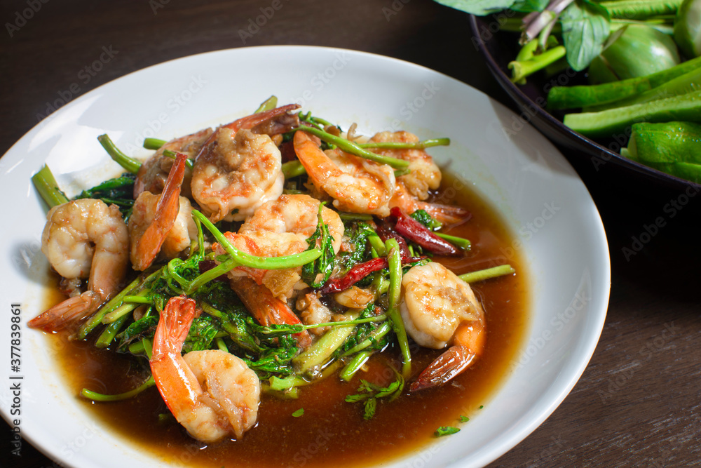 Fried water mimosa with shrimp and oyster sauce in white plate on wooden table Fried water mimosa with shrimp and oyster sauce in white plate on wooden table
