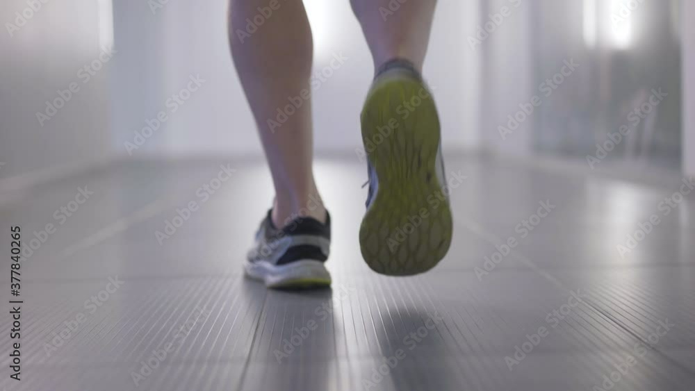 Camera follows feet of male Caucasian athlete walking in gym. Back view close-up legs of confident young man in sneakers strolling indoors. Sport and healthy lifestyle concept. Camera follows feet of male Caucasian athlete walking in gym. Back view close-up legs of confident young man in sneakers strolling indoors. Sport and healthy lifestyle concept.