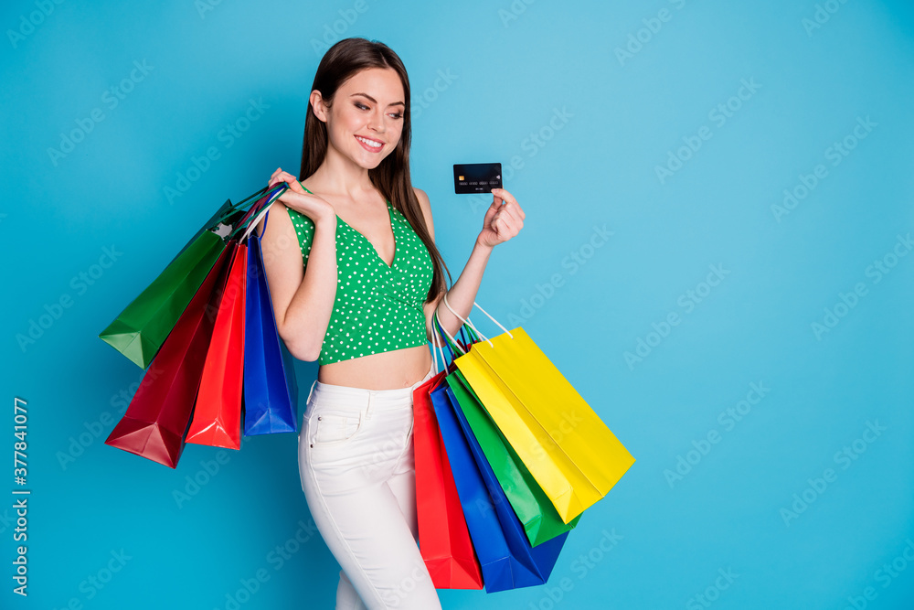 Photo of positive cheerful girl look credit card enjoy pay shopping bags wear white pants trousers tank-top isolated over blue color background Photo of positive cheerful girl look credit card enjoy pay shopping bags wear white pants trousers tank-top isolated over blue color background