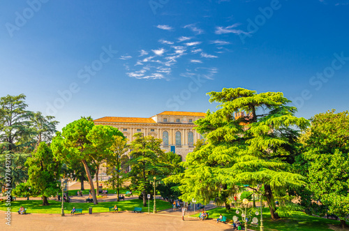 Piazza Bra square in Verona city historical centre with park garden with green cedar and pine trees, Palazzo della Gran Guardia palace building, blue sky background, Veneto Region, Northern Italy
