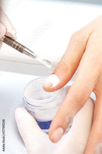 Close up of the process of applying acrylic powder on the nails of a young woman in a beauty salon